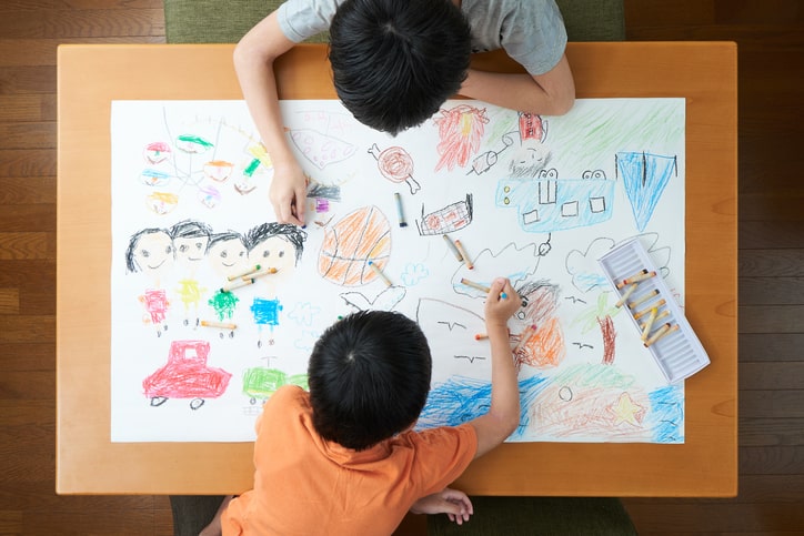 机に画用紙を広げて絵を描いている2人の子供の様子
