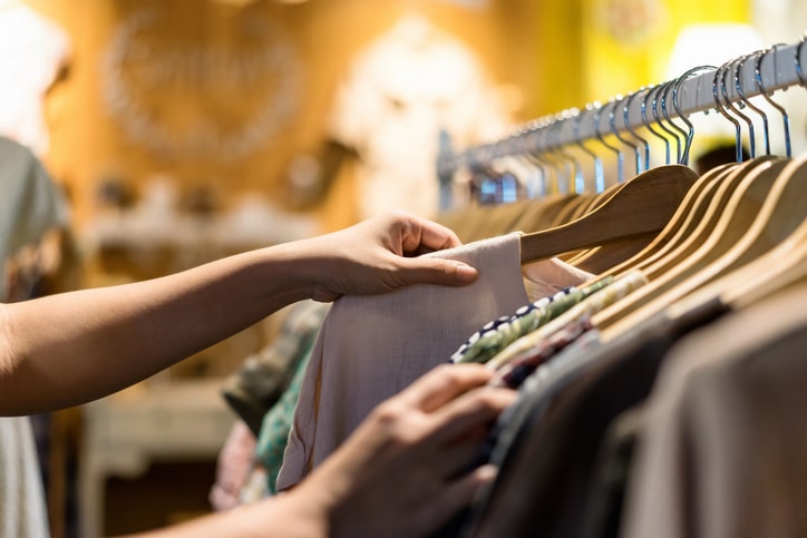 ハンガーラックにかかった服を取る人の画像